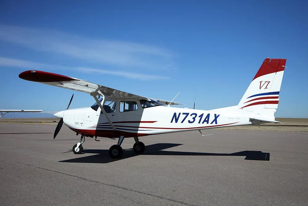 A white and red single-engine propeller aircraft, N731AX, parked on an airfield under a clear blue sky.