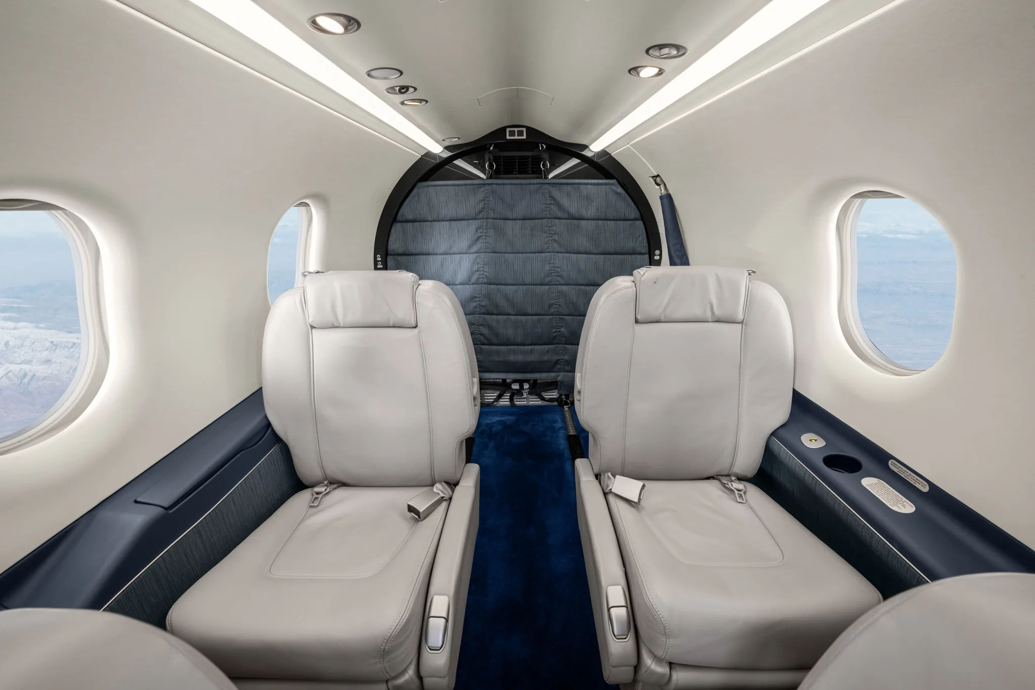 The aircraft's cabin interior shows two light grey leather seats facing a padded rear cargo partition.
