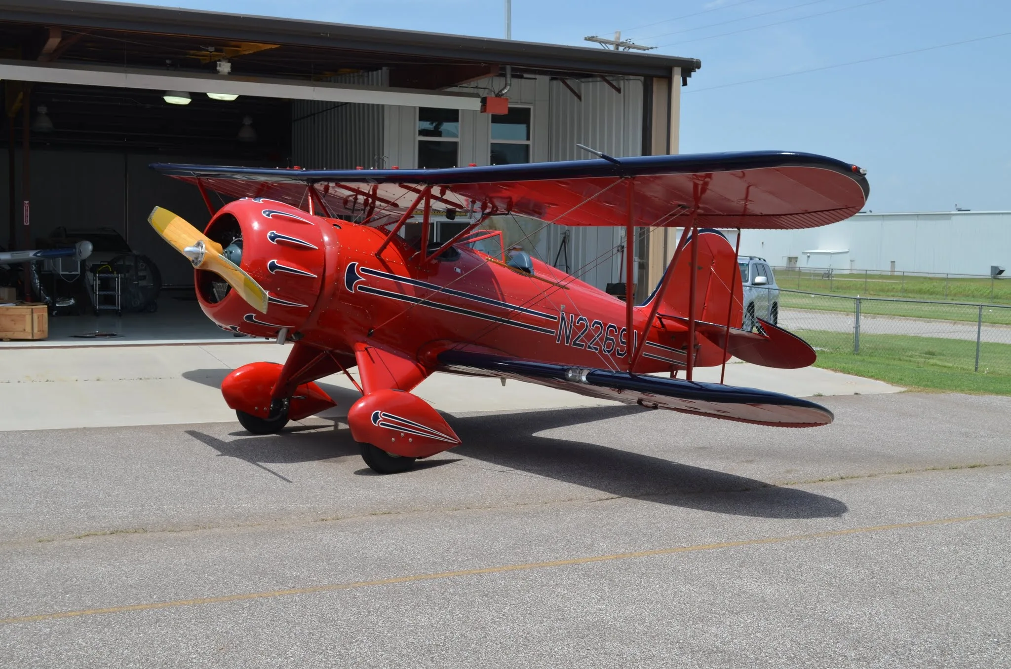 A red biplane N2269V is parked on an asphalt apron in front of an open hangar door.