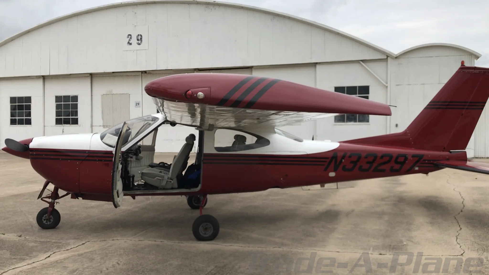 A full side view of the red and white N33297 aircraft with its door open, parked in front of a white hangar.