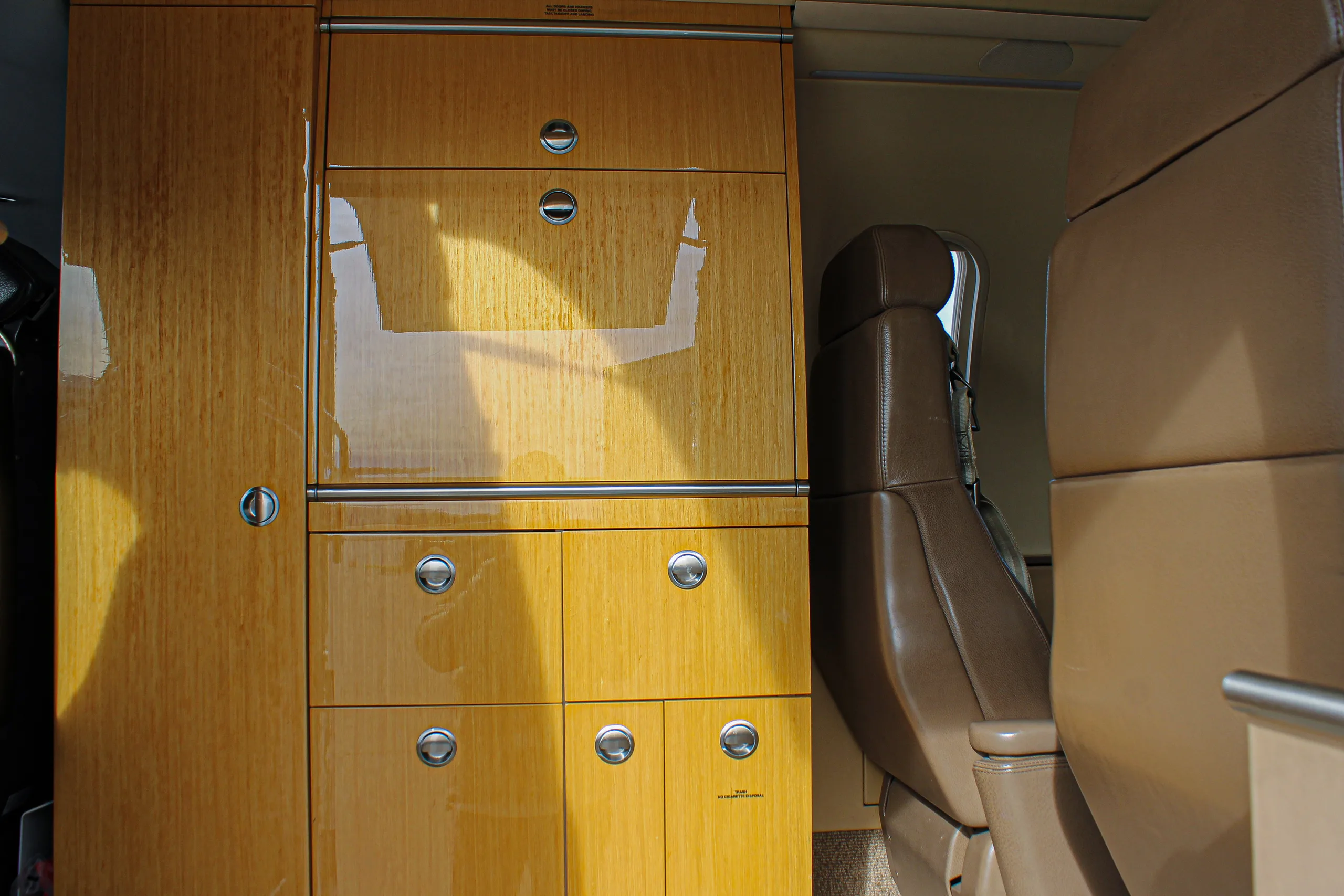 A close-up view of the aircraft's wooden cabinetry and a brown leather seat in the cabin.
