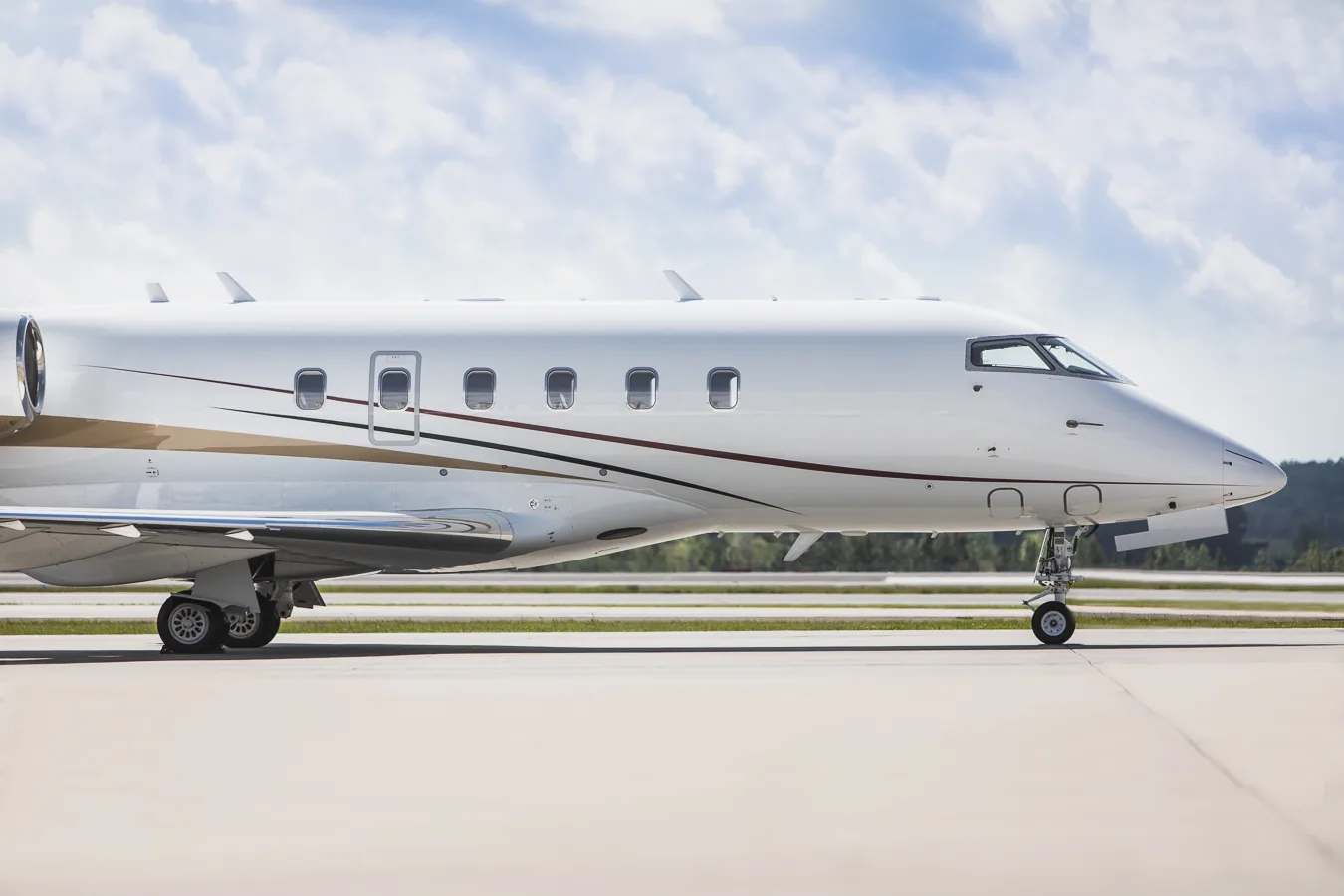 Close-up side view of the fuselage of a white business jet with gold and maroon stripes, parked on an airfield.