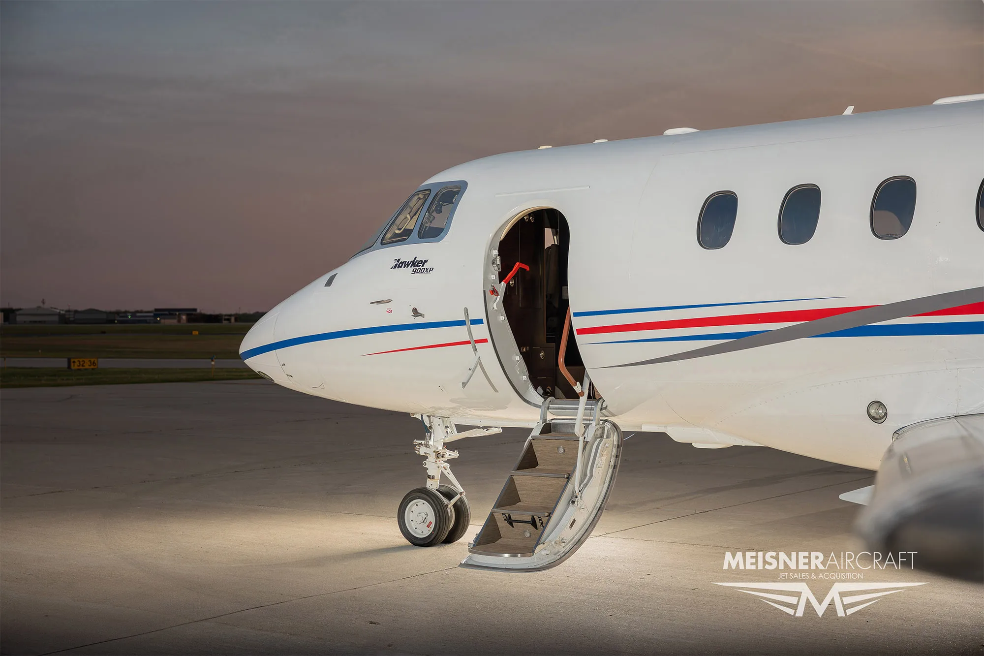 A close-up view of the front fuselage of a white Hawker business jet with its main entry door open and stairs extended.