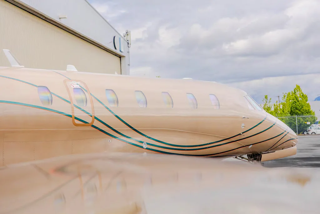 A close-up side view of the beige business jet's fuselage, highlighting the cabin windows and green stripe livery.