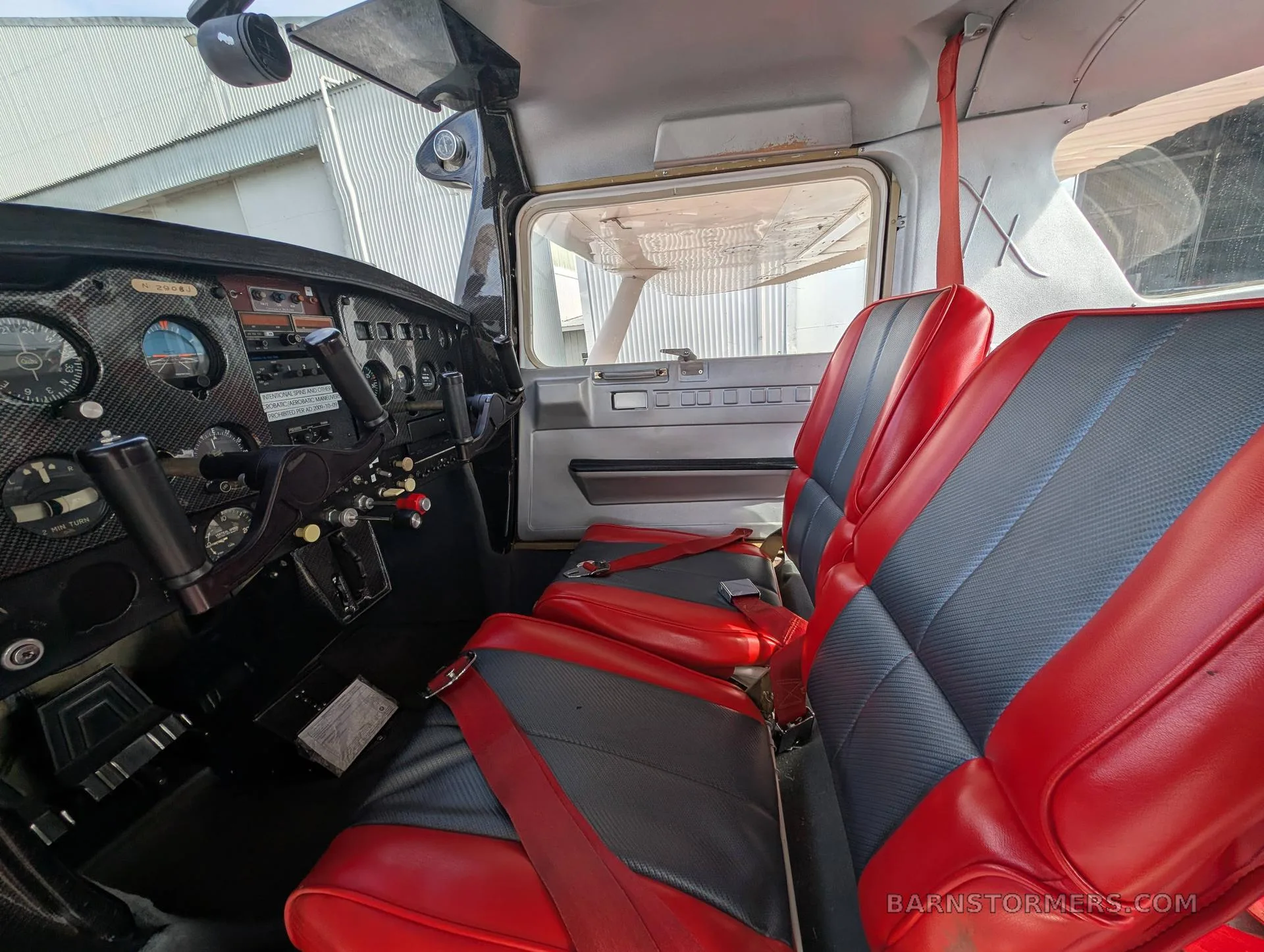The interior of an aircraft cabin with red and grey seats and a partial view of the instrument panel.