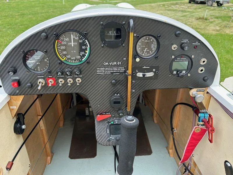 The cockpit instrument panel of a light sport aircraft, featuring analog gauges and a carbon fiber finish.