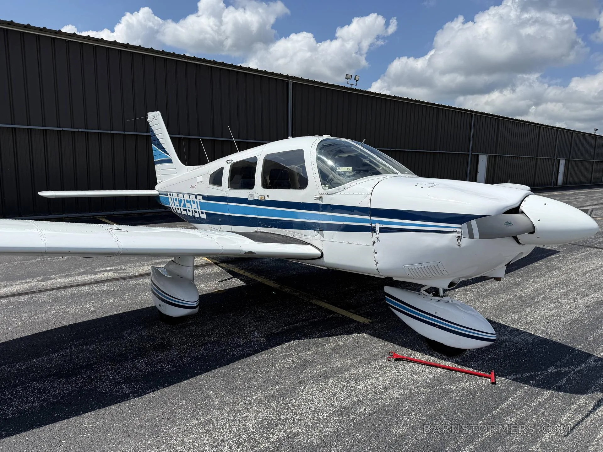 A front-side view of a white Piper aircraft with blue stripes, registration N8268C, parked on an asphalt ramp.