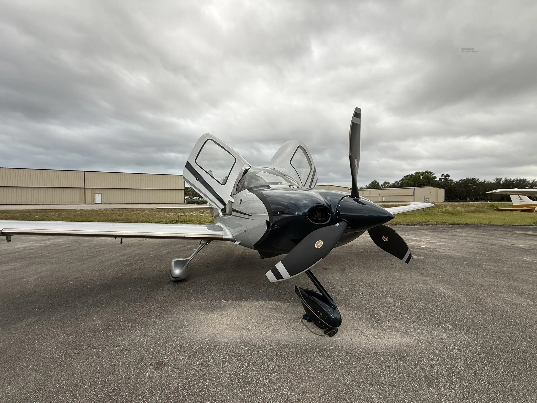 A front-side view of the Cirrus SR22T aircraft, N228CC, with its propeller and open gull-wing doors, parked on an airfield.