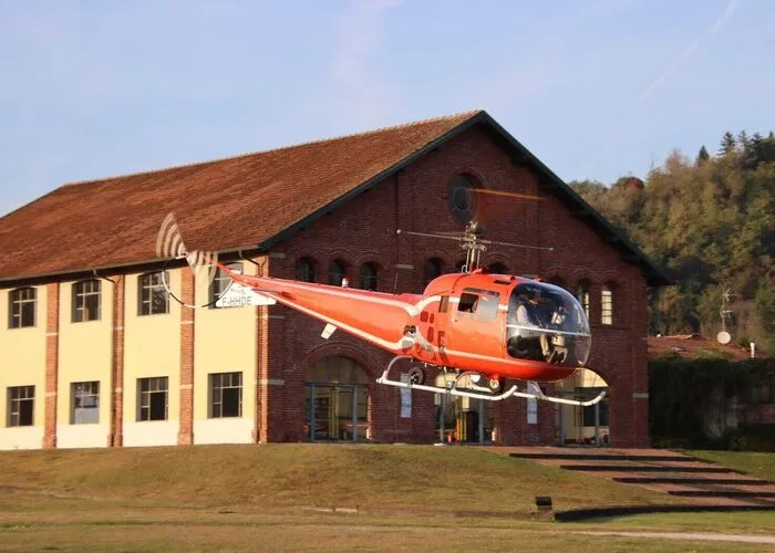 Red helicopter taking off in front of a building.