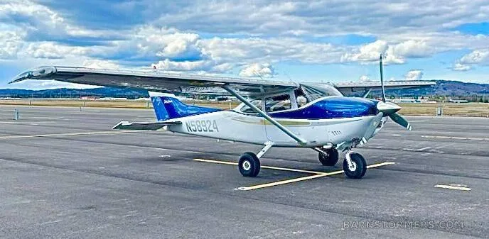 A white and blue Cessna 182 Skylane (N58924) parked on an airfield under a partly cloudy sky.