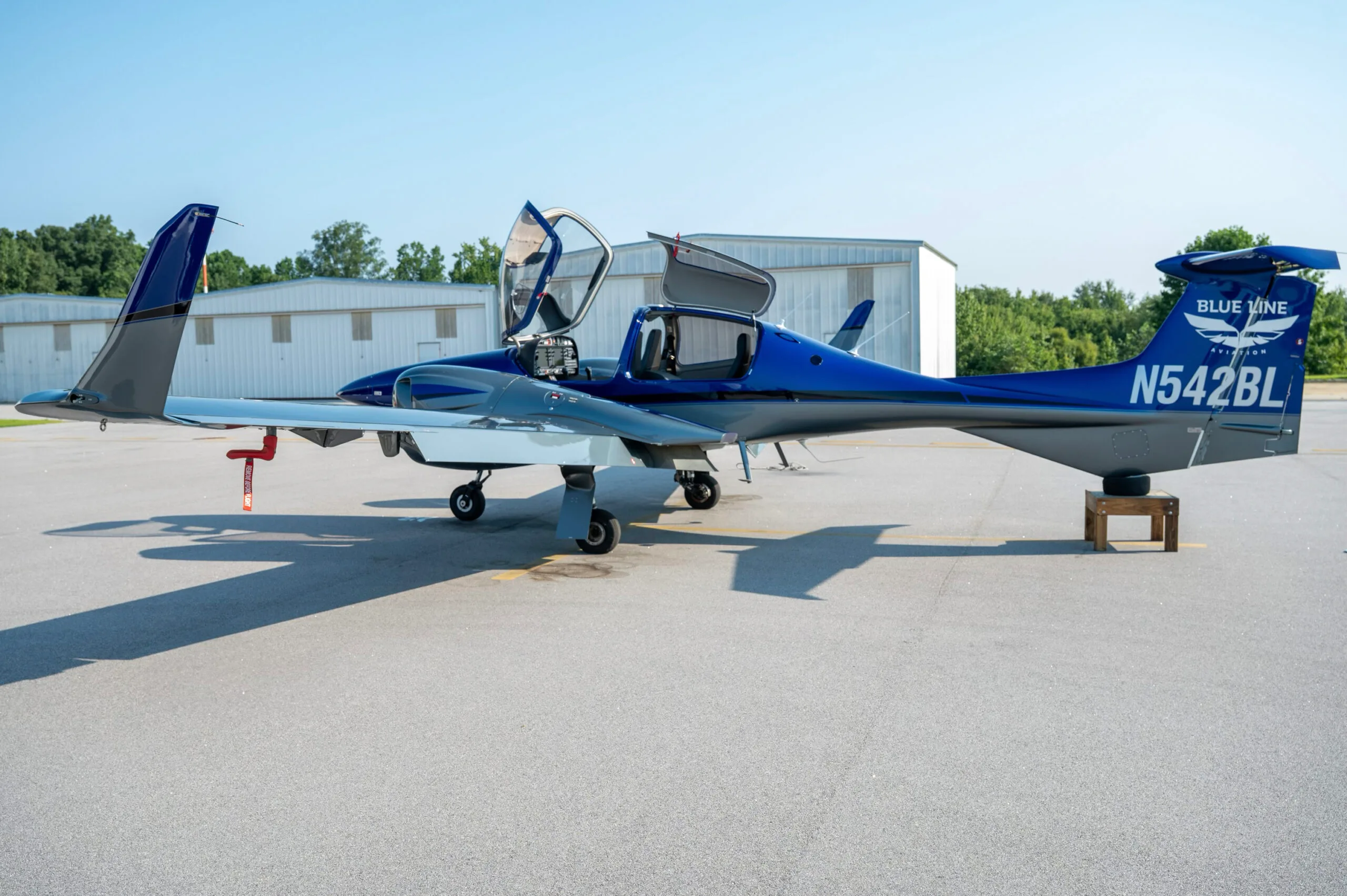 A blue and grey Diamond DA42 aircraft with doors open, parked on an airfield.