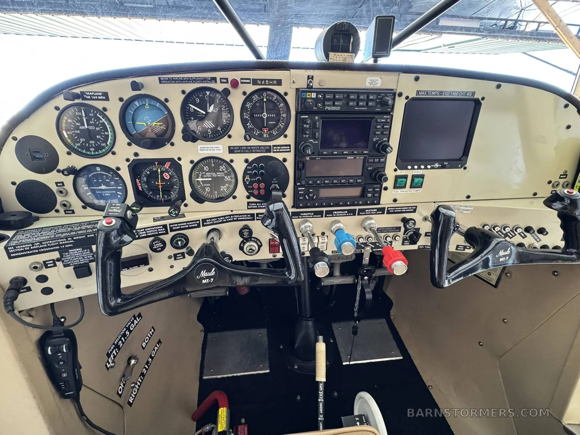 The cockpit of a floatplane, showing the instrument panel with analog gauges and modern avionics, and two control yokes.