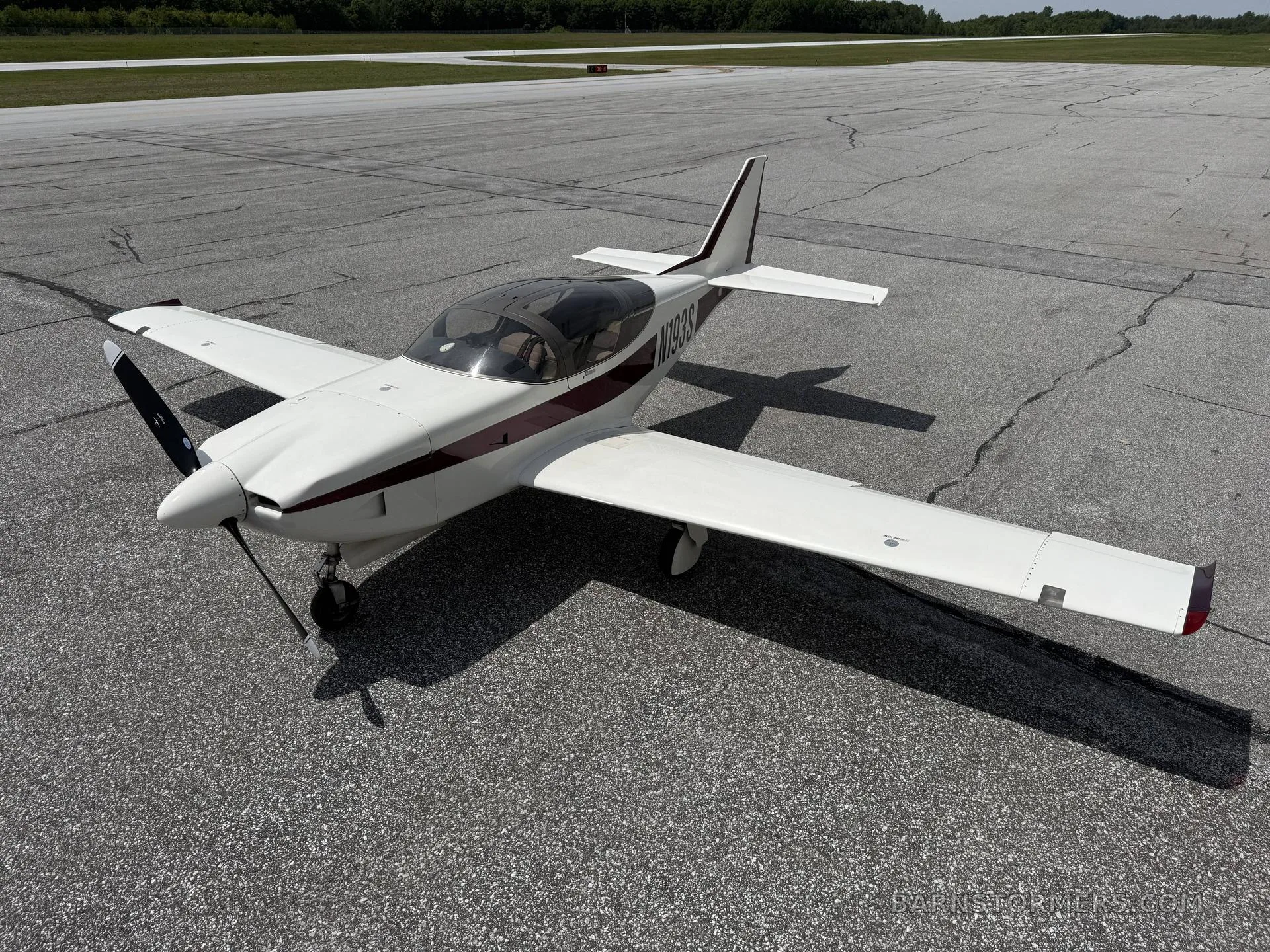 A white and maroon single-engine aircraft (N193S) with a bubble canopy is parked on an asphalt surface, viewed from above and slightly to the front.