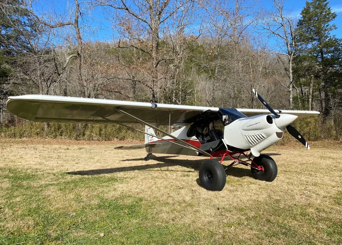 A Carbon Cub aircraft parked on a grassy field with trees in the background.