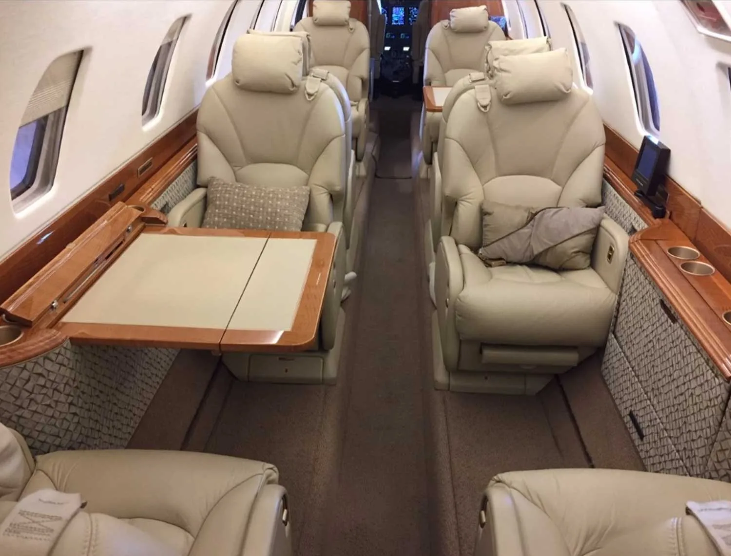 The luxurious interior cabin of a business jet, featuring beige leather seats and wooden tables.
