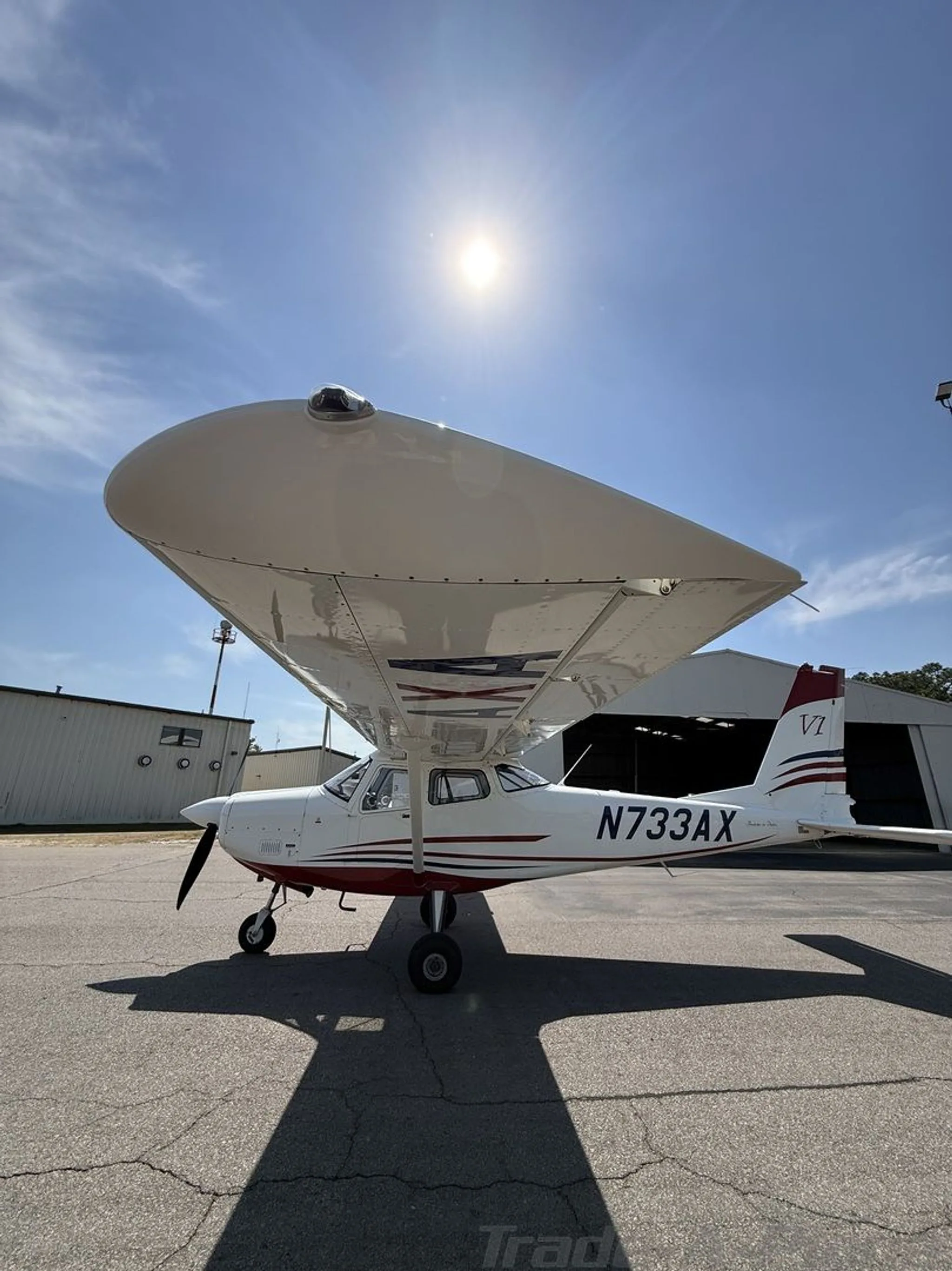 Side view of the white and red single-engine aircraft N733AX with the sun in the background.