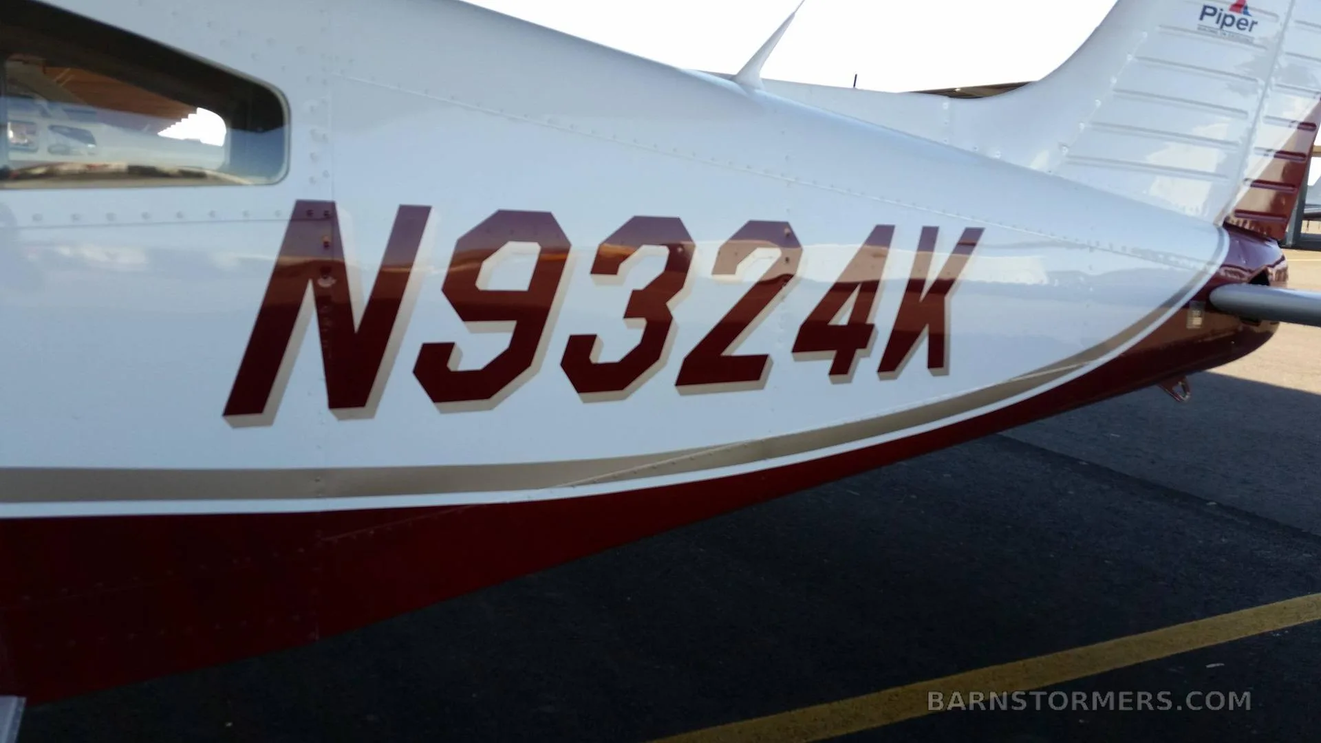 A close-up view of the fuselage of a white and red Piper Archer II, showing the registration number N9324K.
