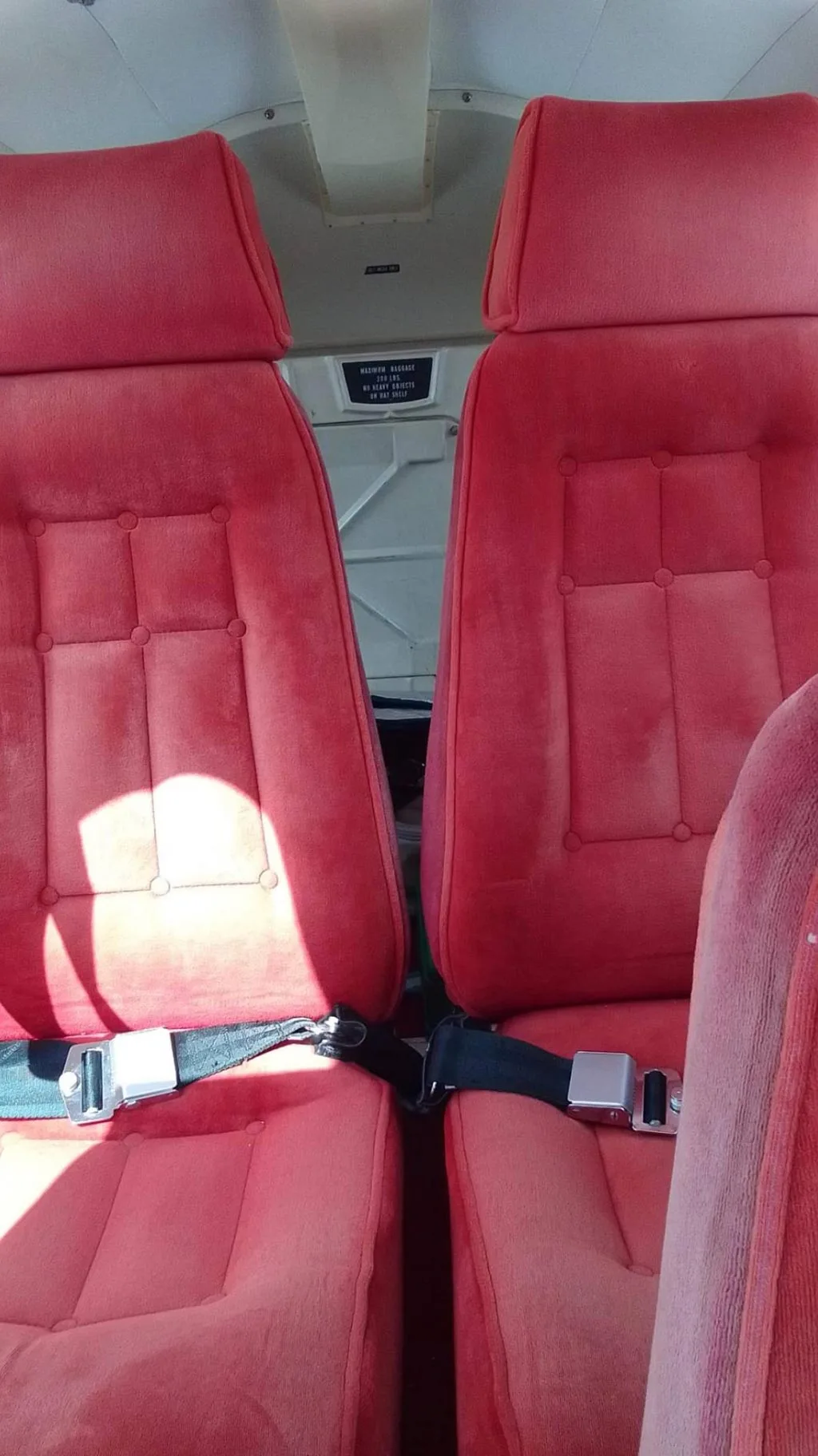 Two red fabric passenger seats with seatbelts in the interior of a small aircraft.