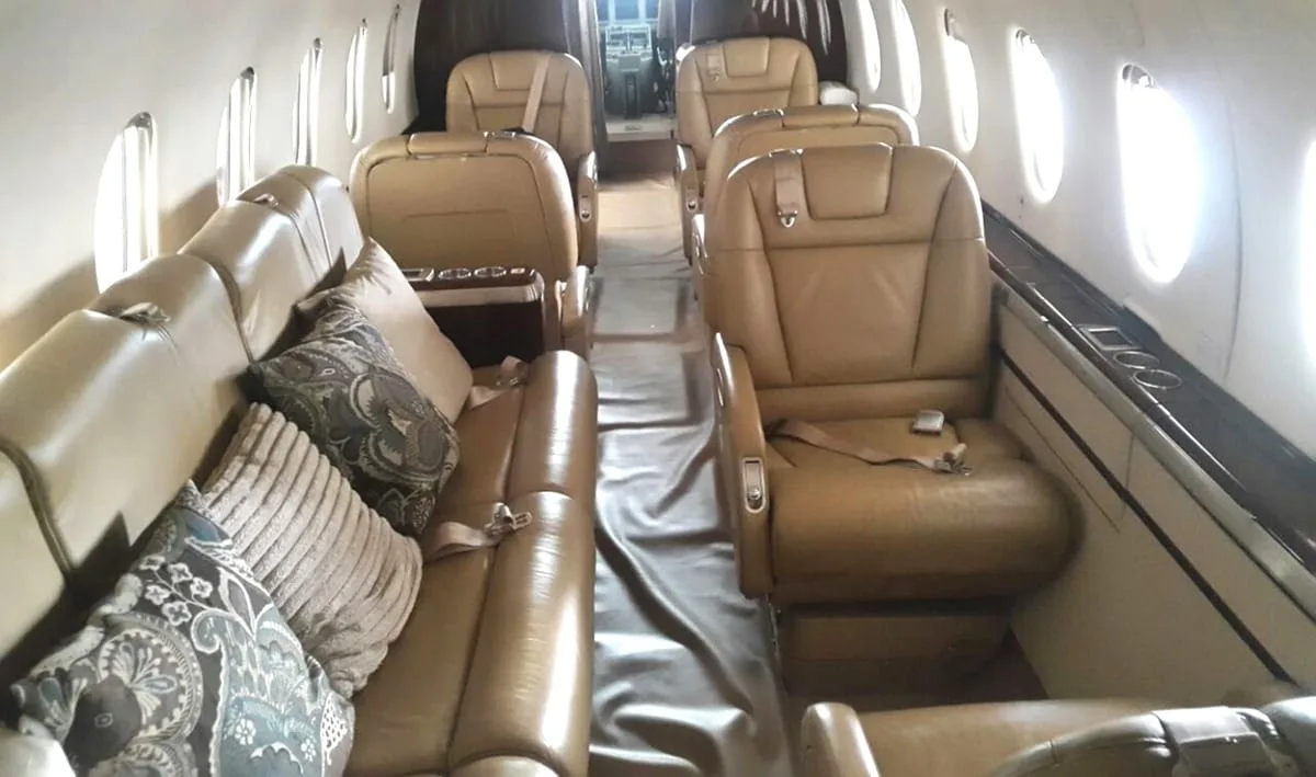 The luxurious interior cabin of a private jet features tan leather seats and decorative pillows.