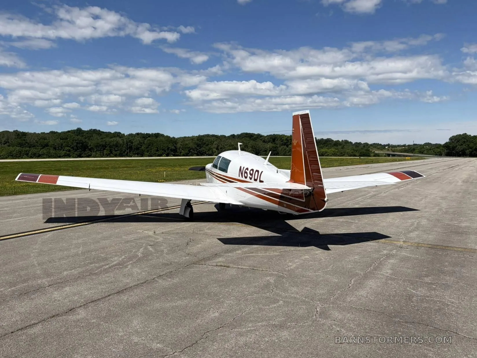 A white and brown Mooney M20J aircraft (N69DL) is parked on an asphalt runway under a partly cloudy sky, viewed from the rear-right side.