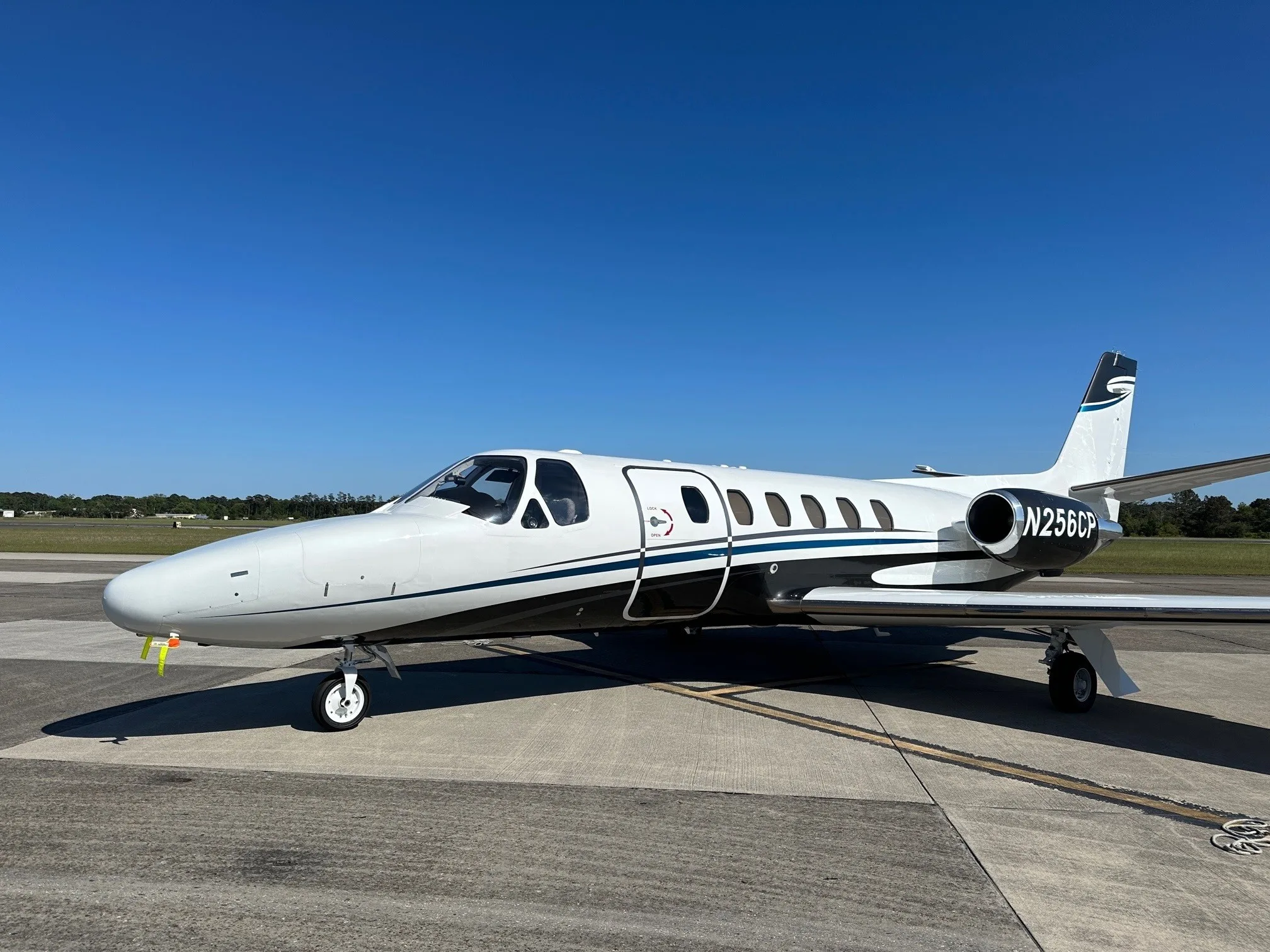 A white and black business jet with blue accent stripes, registration N256CP, parked on an airfield under a clear blue sky.