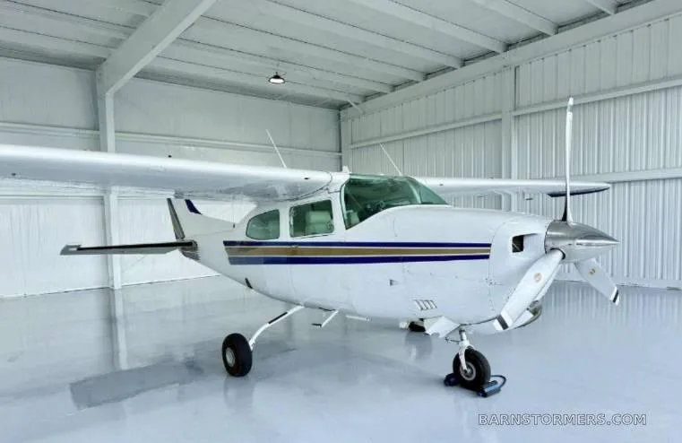 A white single-engine propeller aircraft with blue and gold stripes is parked in a bright hangar.