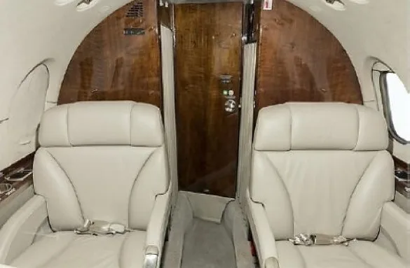 Two light-colored leather seats in a private jet cabin, facing a wooden partition with a door.