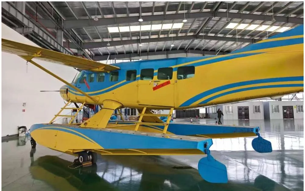 A yellow and blue Cessna Caravan seaplane with Chinese text on the fuselage, viewed from the side-rear in a hangar.