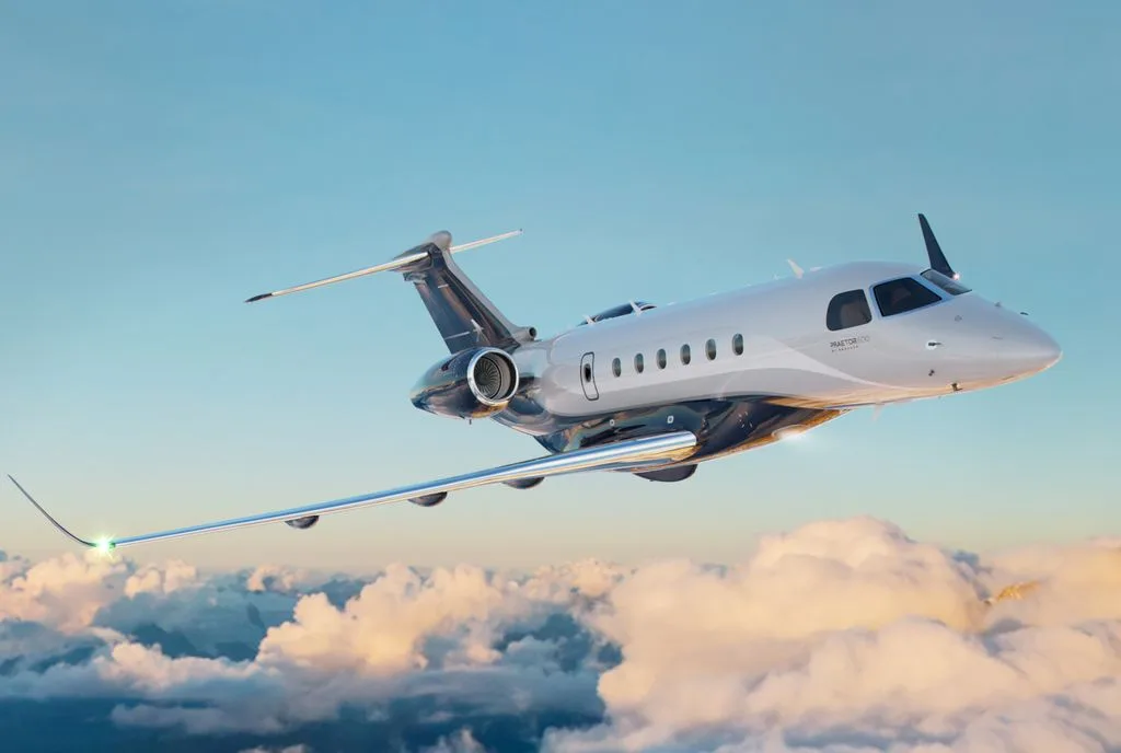 An Embraer Praetor 600 business jet with a grey and dark blue paint scheme flies above the clouds.