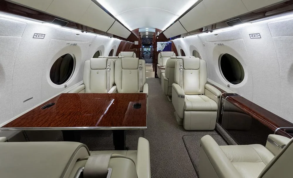 The luxurious interior cabin of a Gulfstream G650 with light leather seats and a polished wood table.
