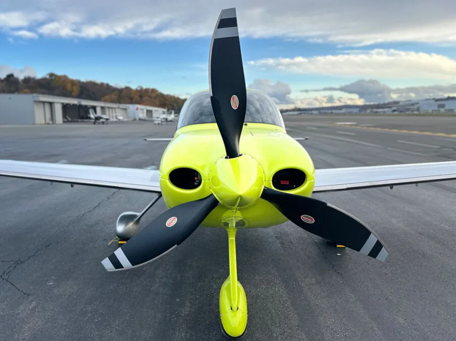 A head-on view of the bright yellow Cirrus SR22 aircraft with its propeller blades visible, parked on an airfield.