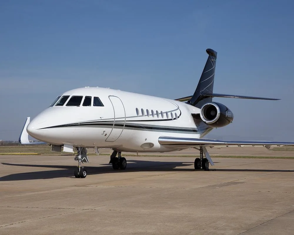 A front-side view of the white Dassault Falcon 900EX business jet with black tail and registration N48RR parked on an airport tarmac.