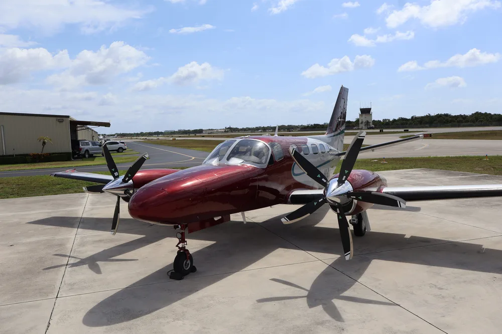 A front-quarter view of the red and silver twin-engine aircraft N441JT on an airfield with a control tower in the background.