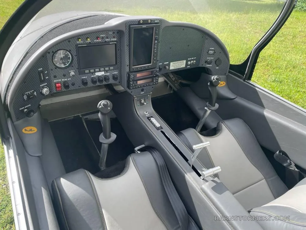 The cockpit of a light sport aircraft, showing the instrument panel with screens and two grey and black seats.