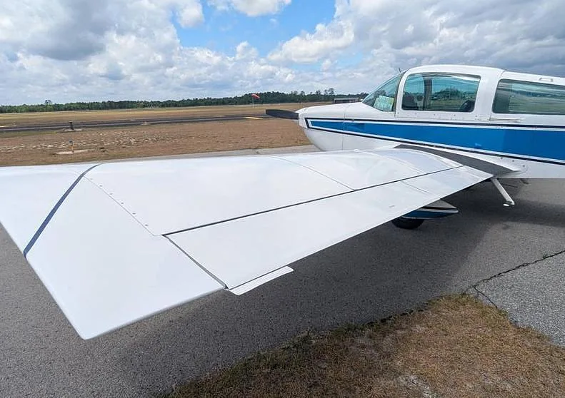A close-up view of the white wing and part of the fuselage of the Grumman AA-5 Traveler N74099 on an airfield.