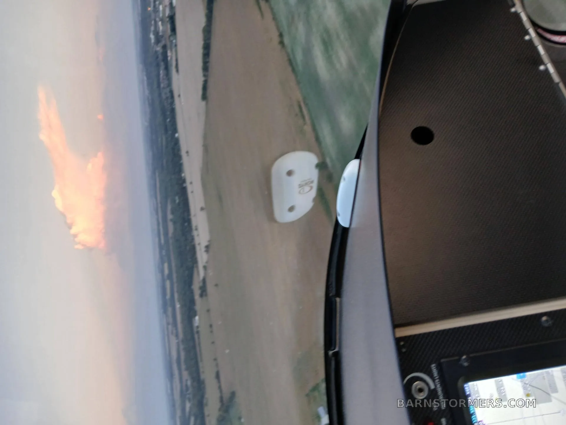 An aerial view from inside a gyrocopter showing fields below and a fiery cloud formation in the distance.