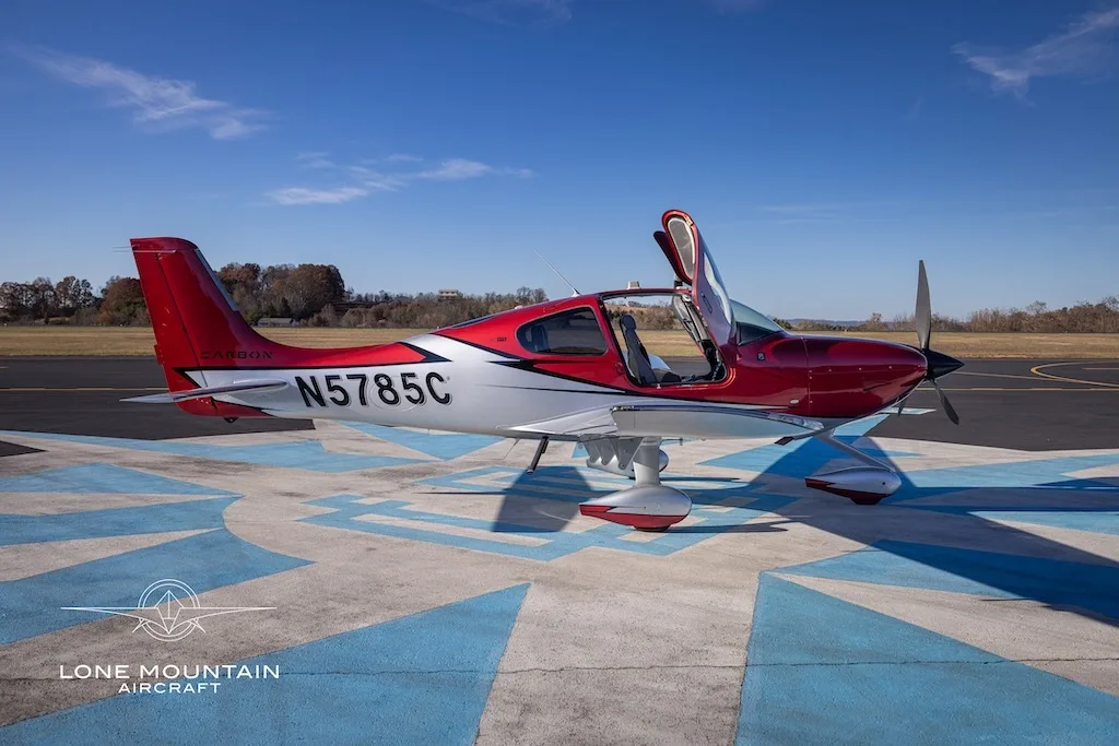 A side view of a red and white Cirrus SR22 aircraft with registration N5785C parked on an airfield with its doors open.