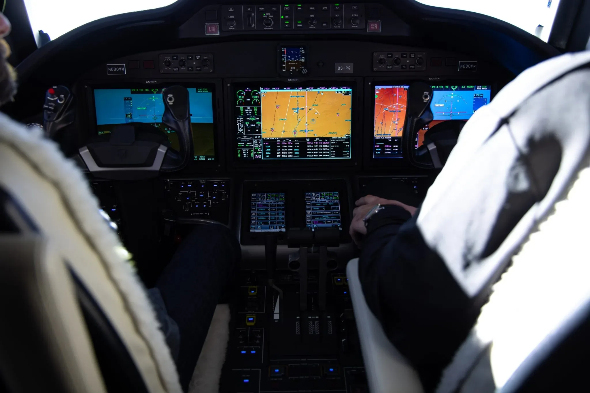 The cockpit features multiple digital displays showing navigation and flight information, with a pilot's hands on the controls.