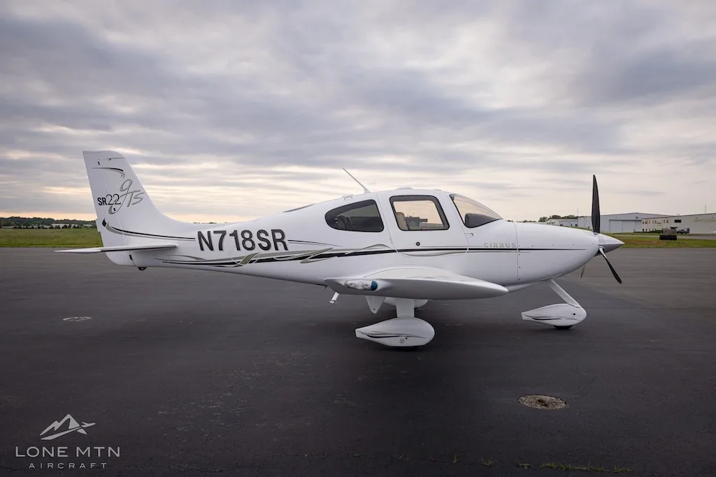Side view of a white Cirrus SR22T aircraft with black and gold accents parked on an asphalt tarmac.
