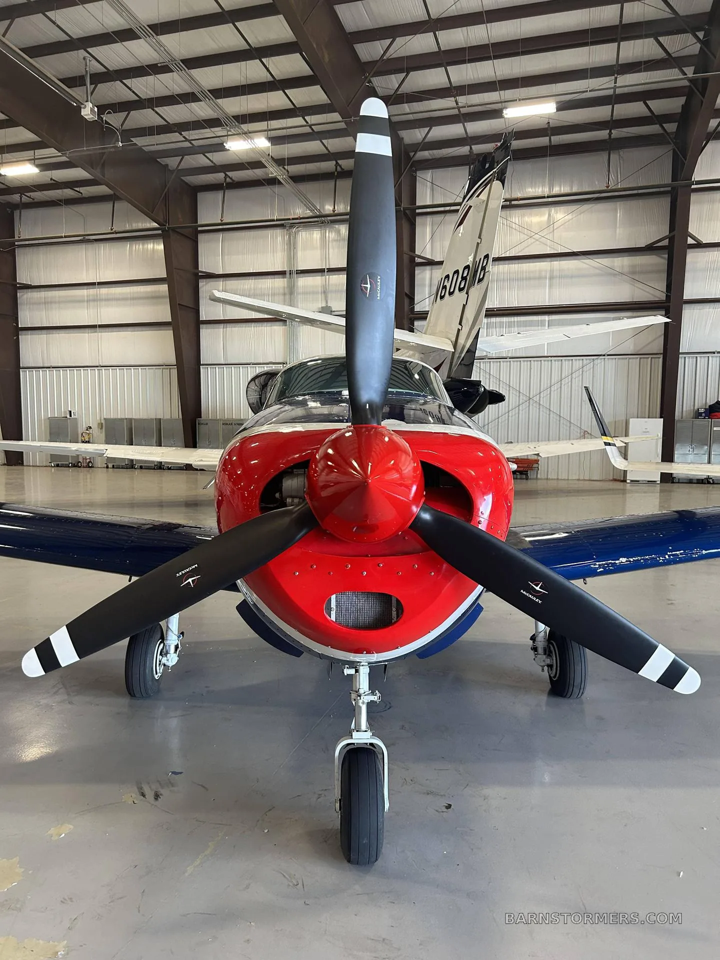 Front view of a blue, white, and red aircraft with a large black propeller, parked in a hangar.