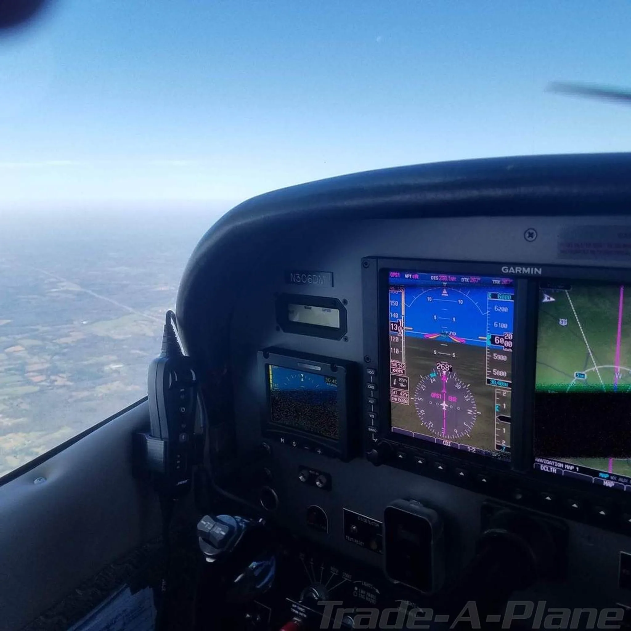 A view from the cockpit showing the instrument panel with a Garmin display and the landscape below.