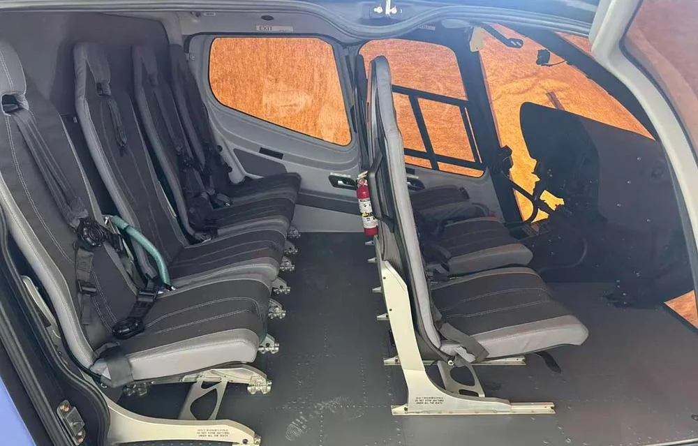 The interior cabin of a helicopter showing multiple grey and black passenger seats and a fire extinguisher.