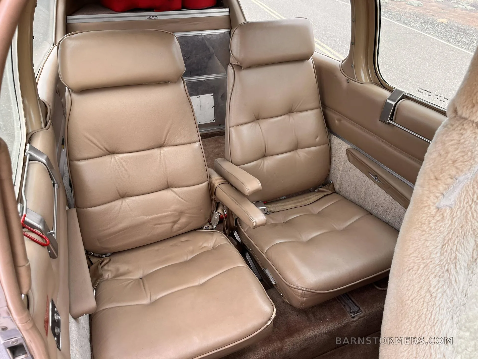 The rear cabin of a Beechcraft Bonanza, featuring two tan leather seats with armrests.