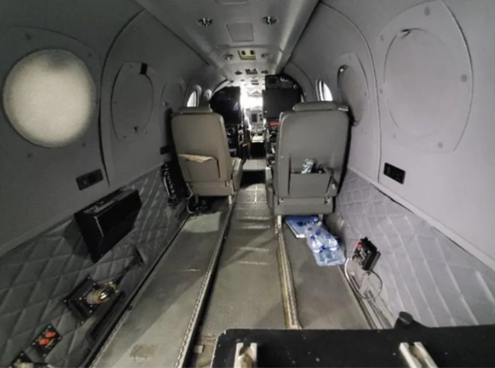 The interior cabin of an aircraft shows two grey seats facing forward towards the cockpit, with quilted side panels.