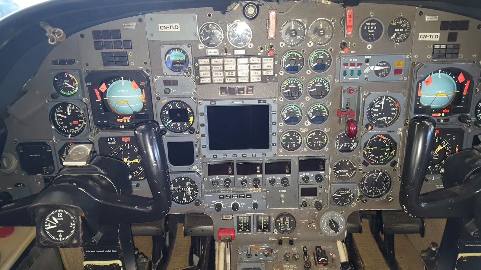 The cockpit instrument panel of a business jet, featuring numerous analog gauges, digital displays, and control yokes.