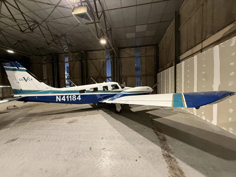 Left side view of a Piper Seneca aircraft N41184, with white and blue livery, inside a hangar.