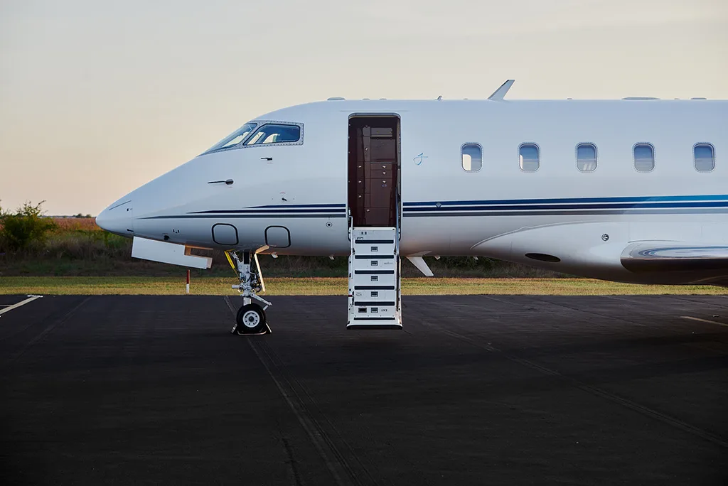 A side view of the front fuselage of a white private jet with its entry door and stairs extended.