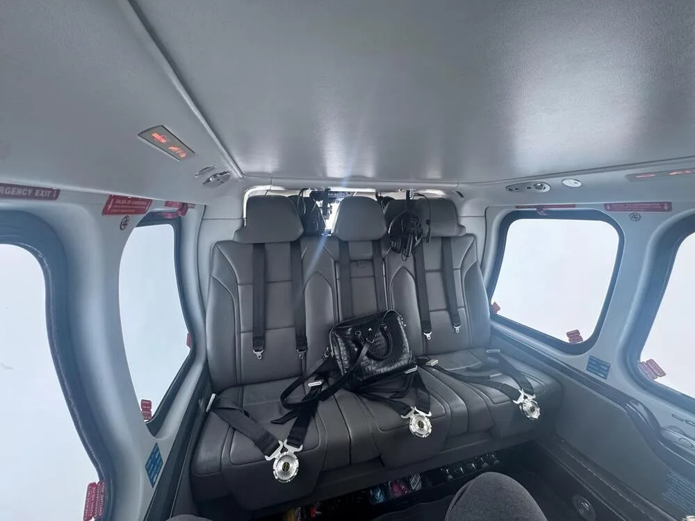 The grey leather passenger seats of a helicopter cabin are visible, with a black handbag resting on one seat.