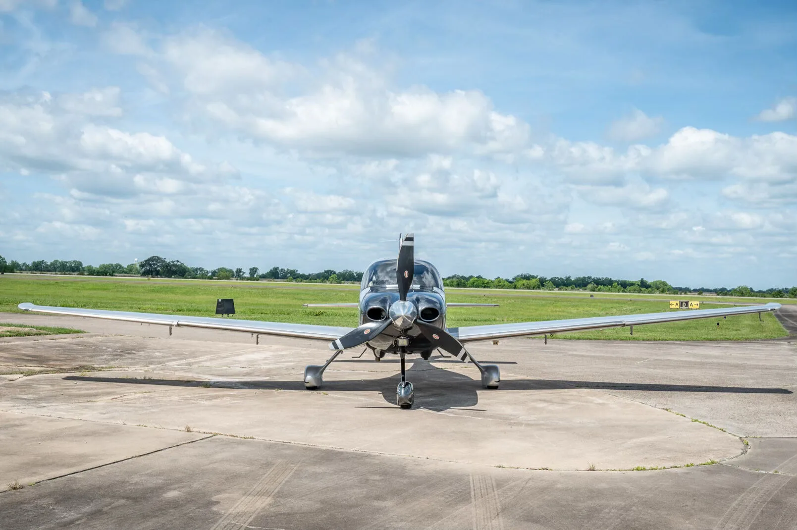 A front view of the silver and black Cirrus SR22T GTS Platinum aircraft N219TW parked on an airfield under a cloudy sky.