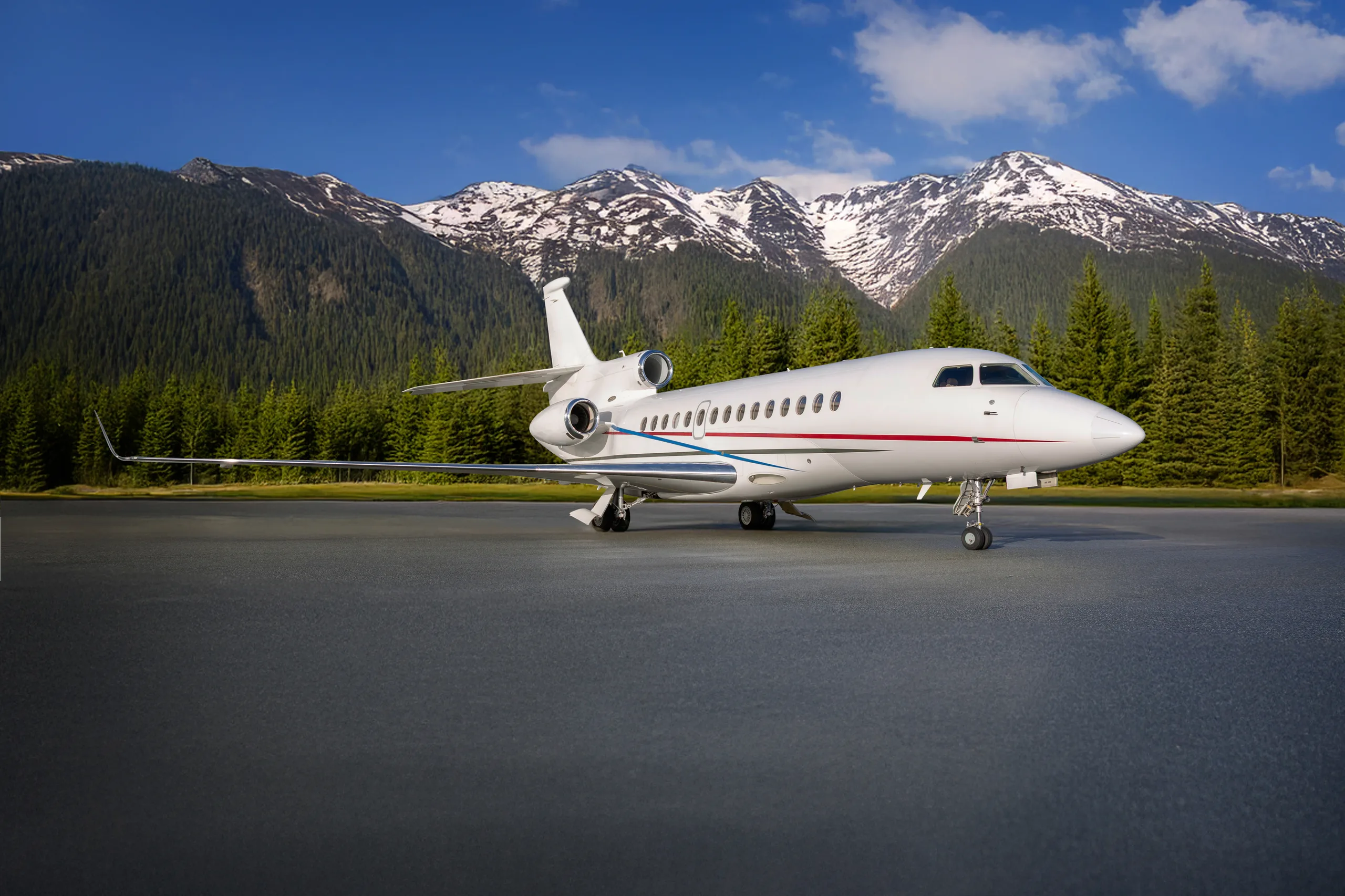 A Falcon jet parked on the tarmac with mountains in the background.